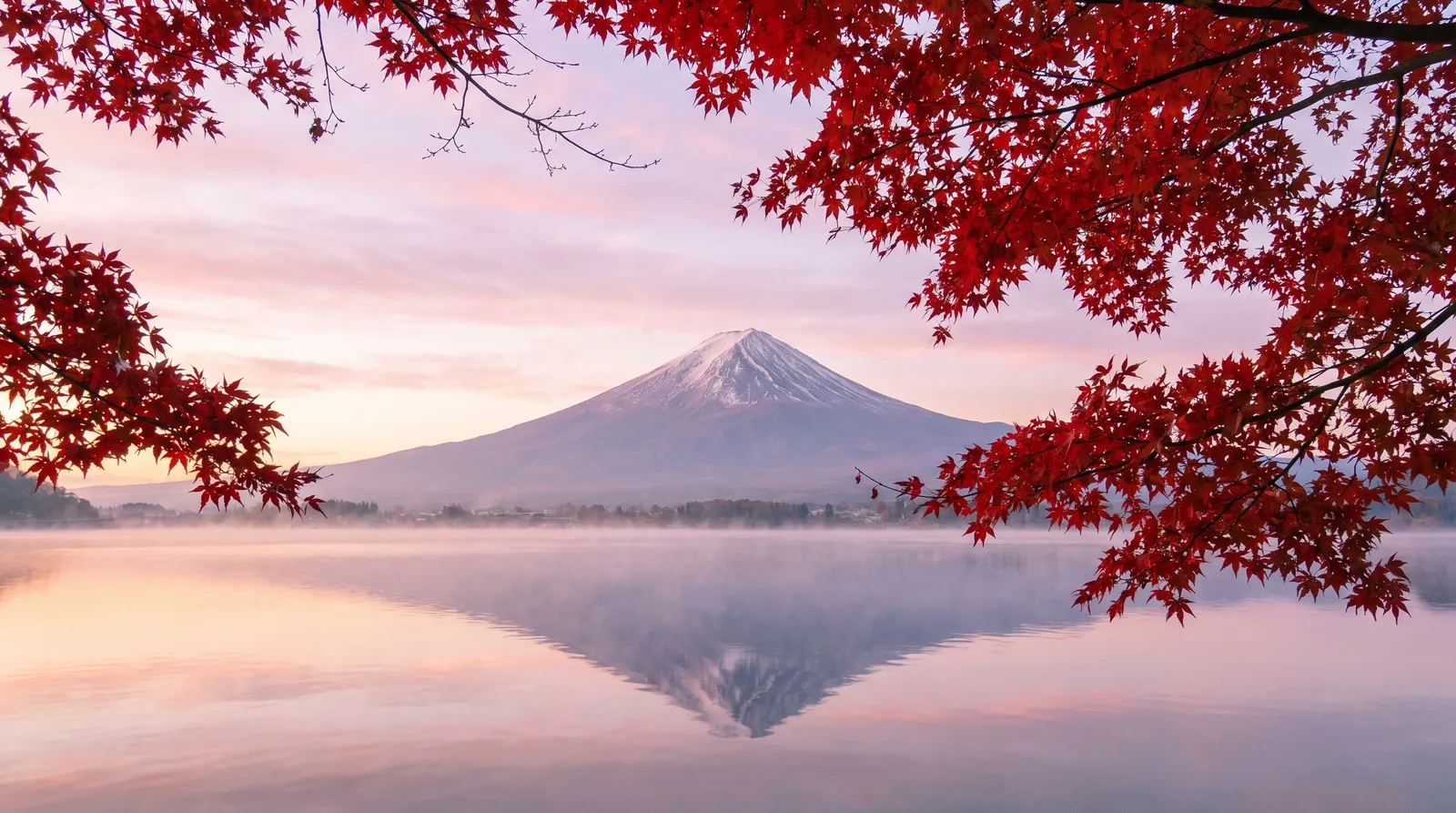 Mount Fuji reflected in Lake Kawaguchi on a still autumn morning, red maple leaves framing the foreground, thin mist on the water, soft pastel sky, landscape photography