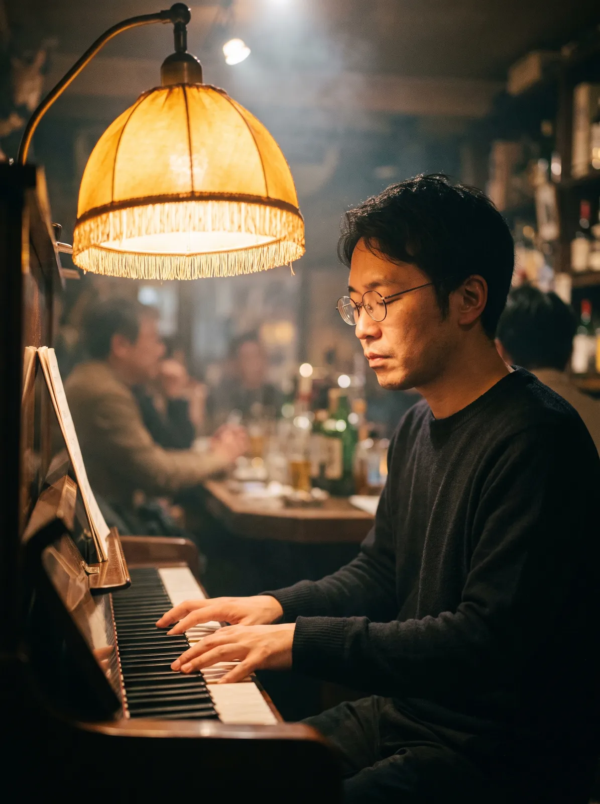 Japanese jazz pianist in his thirties playing in a tiny Tokyo bar, eyes closed, round glasses, warm amber lamp over the piano, light stage haze, shallow focus on his hands and face, Leica look