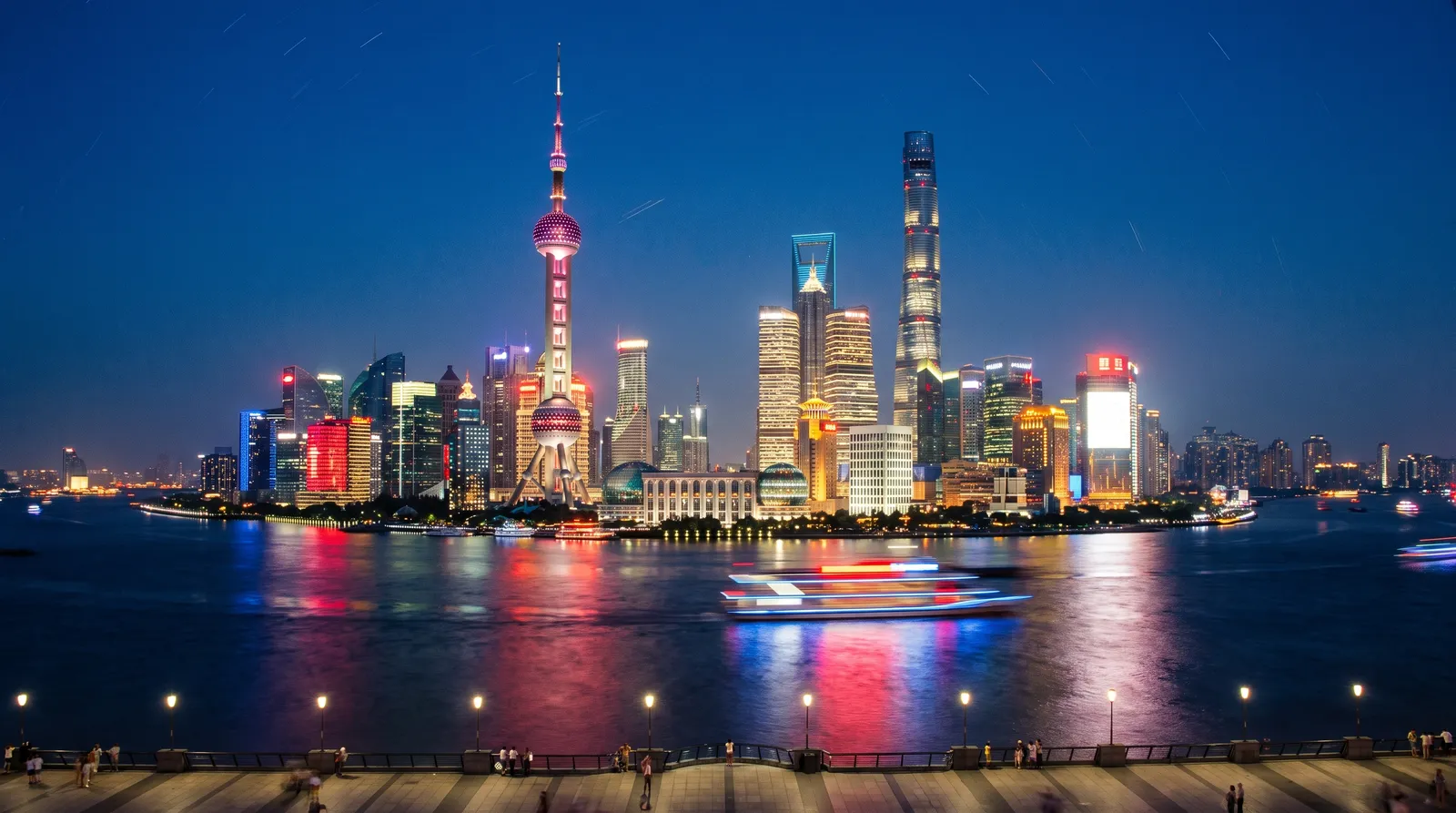 Shanghai Lujiazui skyline across the Huangpu River at night, illuminated towers reflected in the water, a tour boat gliding past, crisp long exposure