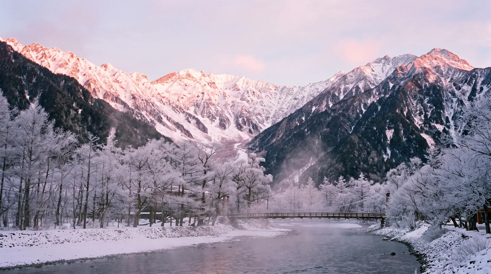 Japanese Alps in winter at sunrise, the snow-covered peaks of Kamikochi glowing pink, the Azusa river steaming in the cold, frosted trees