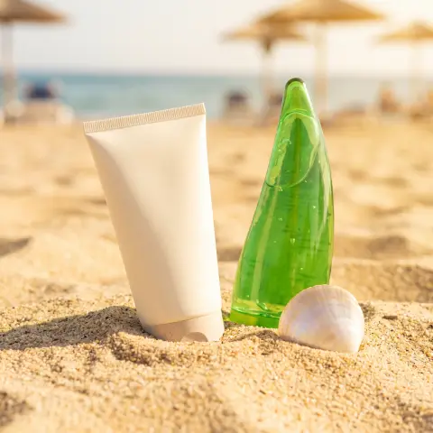 Sunscreen tube and aloe gel on a sandy beach with a seashell, bright sunlight, summer skincare ad