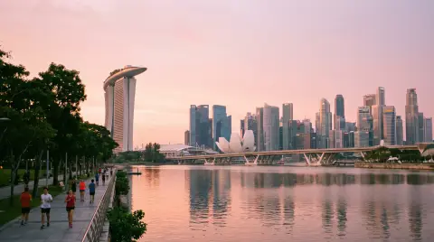 Singapore Marina Bay at sunrise from the waterfront, calm water, soft pink sky, joggers along the promenade, clean moder
