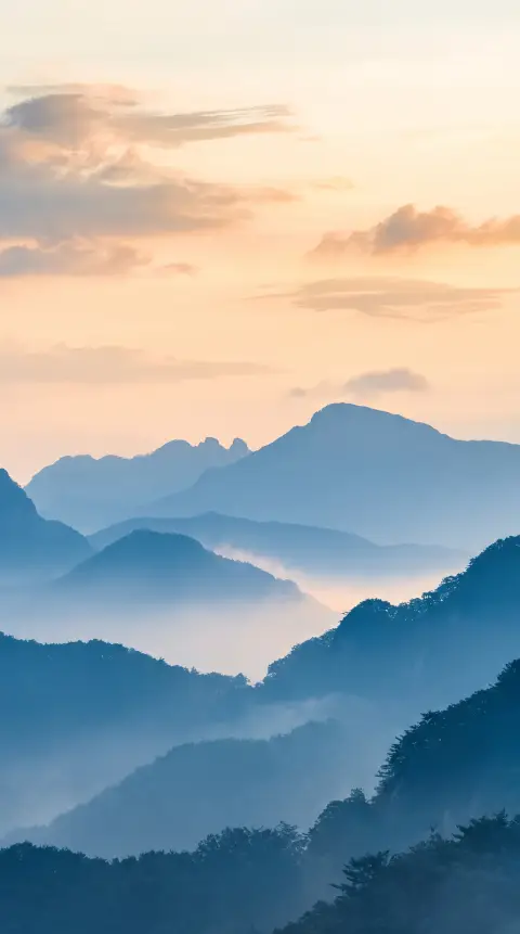 Vertical wallpaper of a misty Korean mountain ridge at sunrise, layered blue silhouettes, ink-painting feeling, photorea