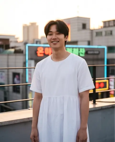 Portrait of a young Japanese man wearing a white summer dress in a Seoul rooftop at golden hour, neon rim light, candid 