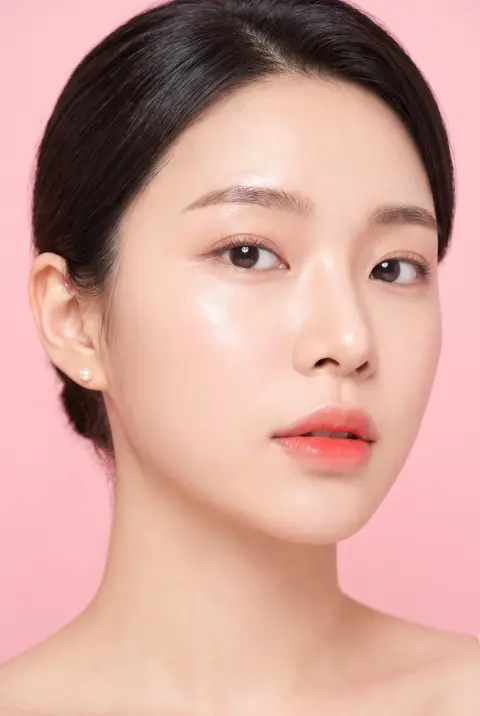 Close-up beauty shot of a model with glass-skin makeup, coral gradient lips and a single pearl earring, soft beauty-dish