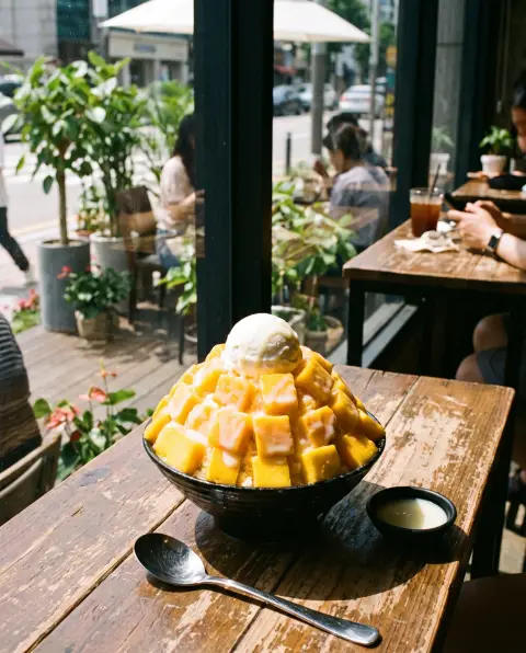 Korean mango bingsu piled high with mango cubes, condensed milk and a scoop of yogurt ice cream on a summer café table…
