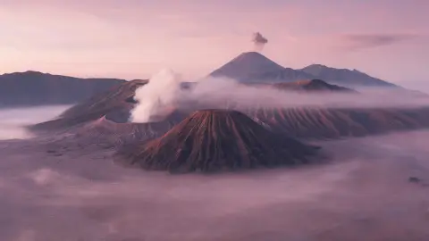 Mount Bromo in East Java at dawn from a high viewpoint, the smoking crater rising from a sea of sand and mist…