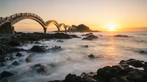 Sanxiantai on Taiwan's east coast at sunrise, a long multi-arched footbridge curving out to a rocky islet…