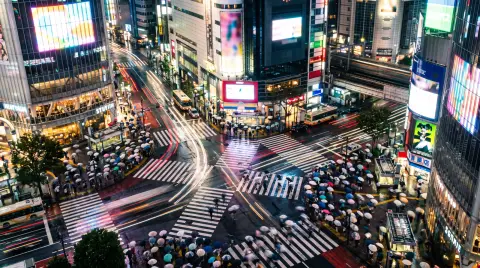 Tokyo Shibuya scramble crossing at night seen from above, long exposure light trails, hundreds of umbrellas in light rai