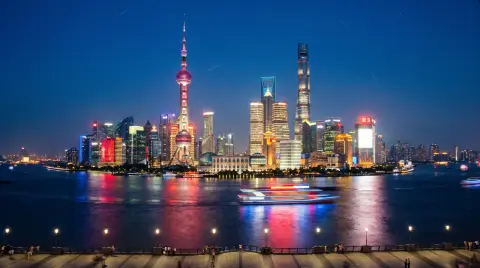 Shanghai Lujiazui skyline across the Huangpu River at night, illuminated towers reflected in the water, a tour boat glid