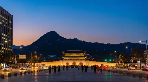 Seoul Gwanghwamun square at dusk with the palace gate and Bugaksan mountain behind, city lights coming on