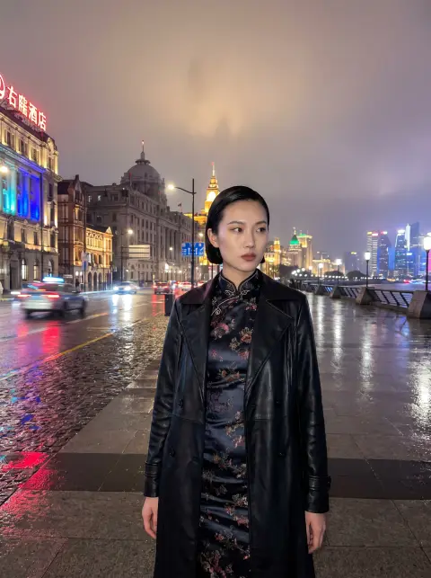 Shanghai model in a reinterpreted silk qipao with a leather trench layered over it, standing on the Bund at night, wet p