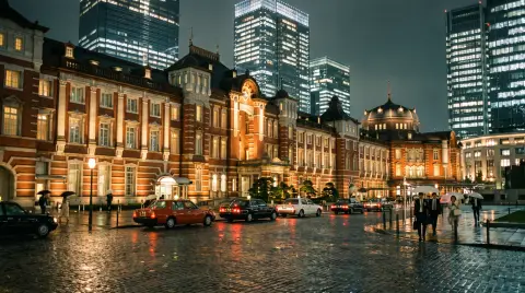 Tokyo Station Marunouchi red brick building at night with modern towers behind, illuminated facade, taxis waiting, elega
