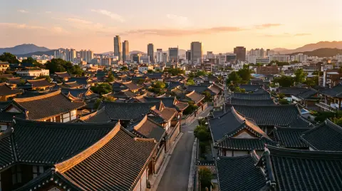 Jeonju hanok village rooftops at sunset viewed from a hill, hundreds of curved tile roofs, warm light, modern city beyon
