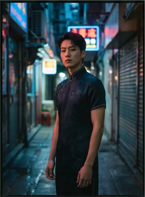 High fashion editorial of a young Chinese man wearing a modern qipao in a Hong Kong neon alley, moody low key lighting,