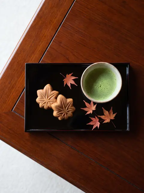 Food photography: Japanese mooncake-style momiji manju and matcha on a lacquer tray with maple leaves…